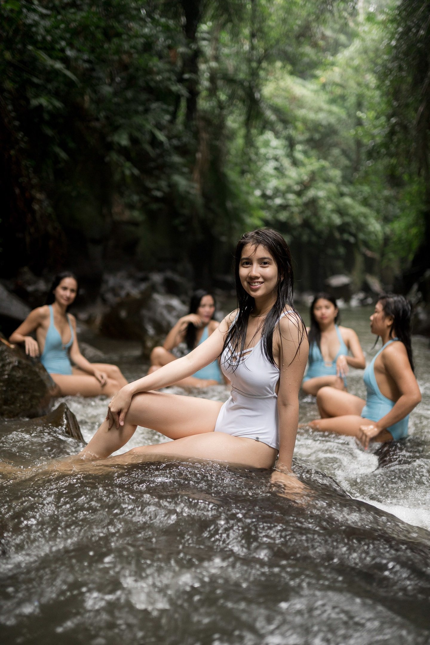 Friends portrait sitting together in shallow river at Kanto Lampo Waterfall Bali