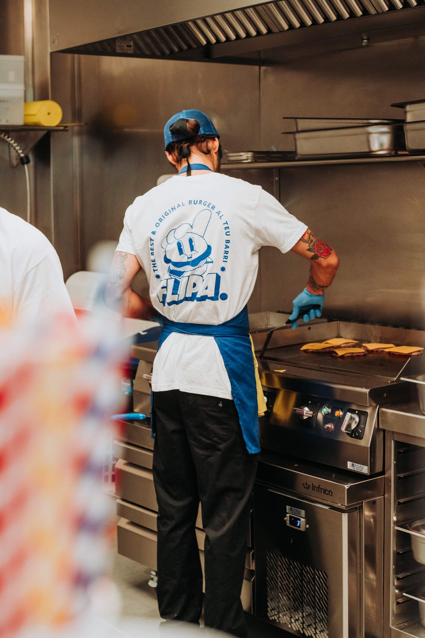 Cuiner de Flipa Burger preparant hamburgueses a la planxa amb l’uniforme de la marca