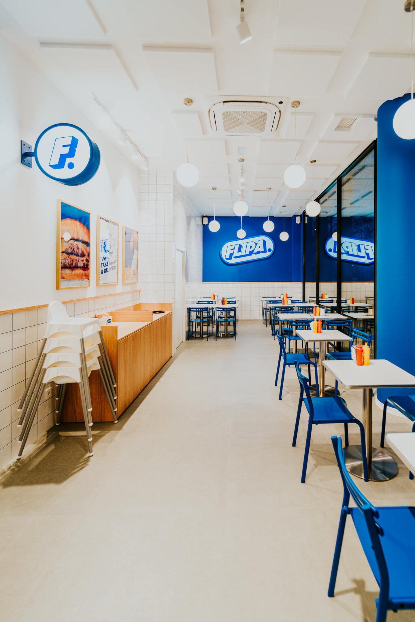 Vista de l’interior de Flipa Burger amb logotip a la paret blava, decoració retro i ambient lluminós