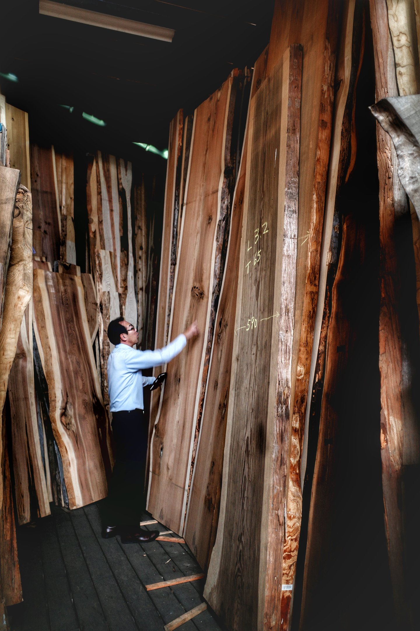 A woodworking professional inspects large live edge wood slabs in a lumber warehouse.