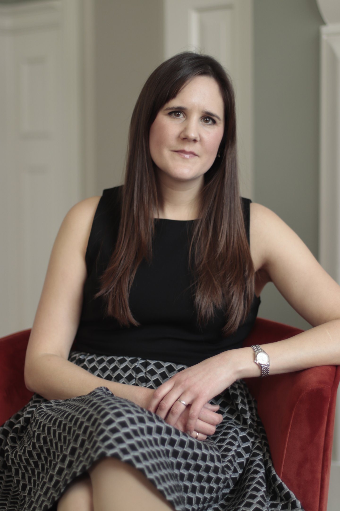 Photo of Anna Joyce, CBTI insomnia therapist in UK, sitting in red chair wearing a black dress