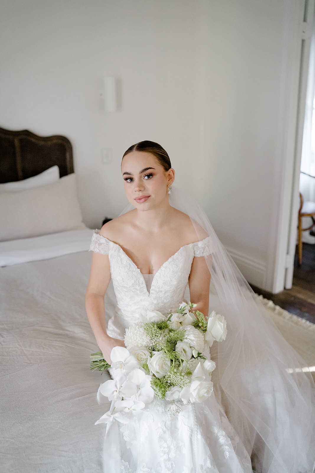 a bride in a white wedding dress sitting on a bed