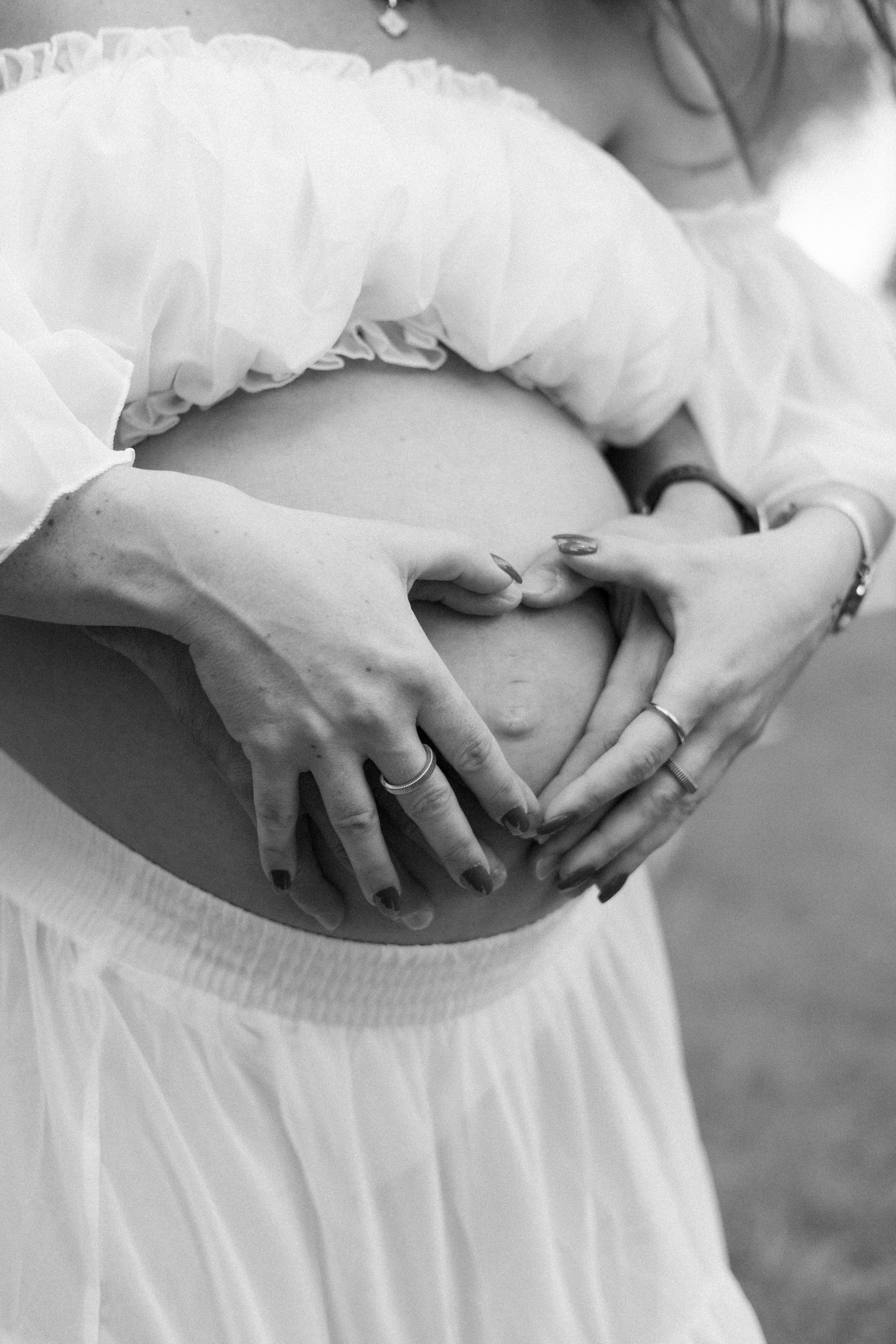 Detall de la panxa d'una dona embarassada formant un cor amb les mans en una sessió de maternitat 