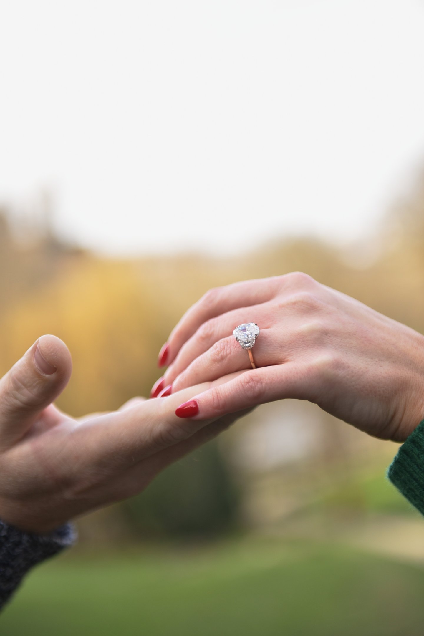 gros plan sur un main d'homme soulevant la main d'une femme portant une bague de fiançailles, le fond est lumineux et flou.
