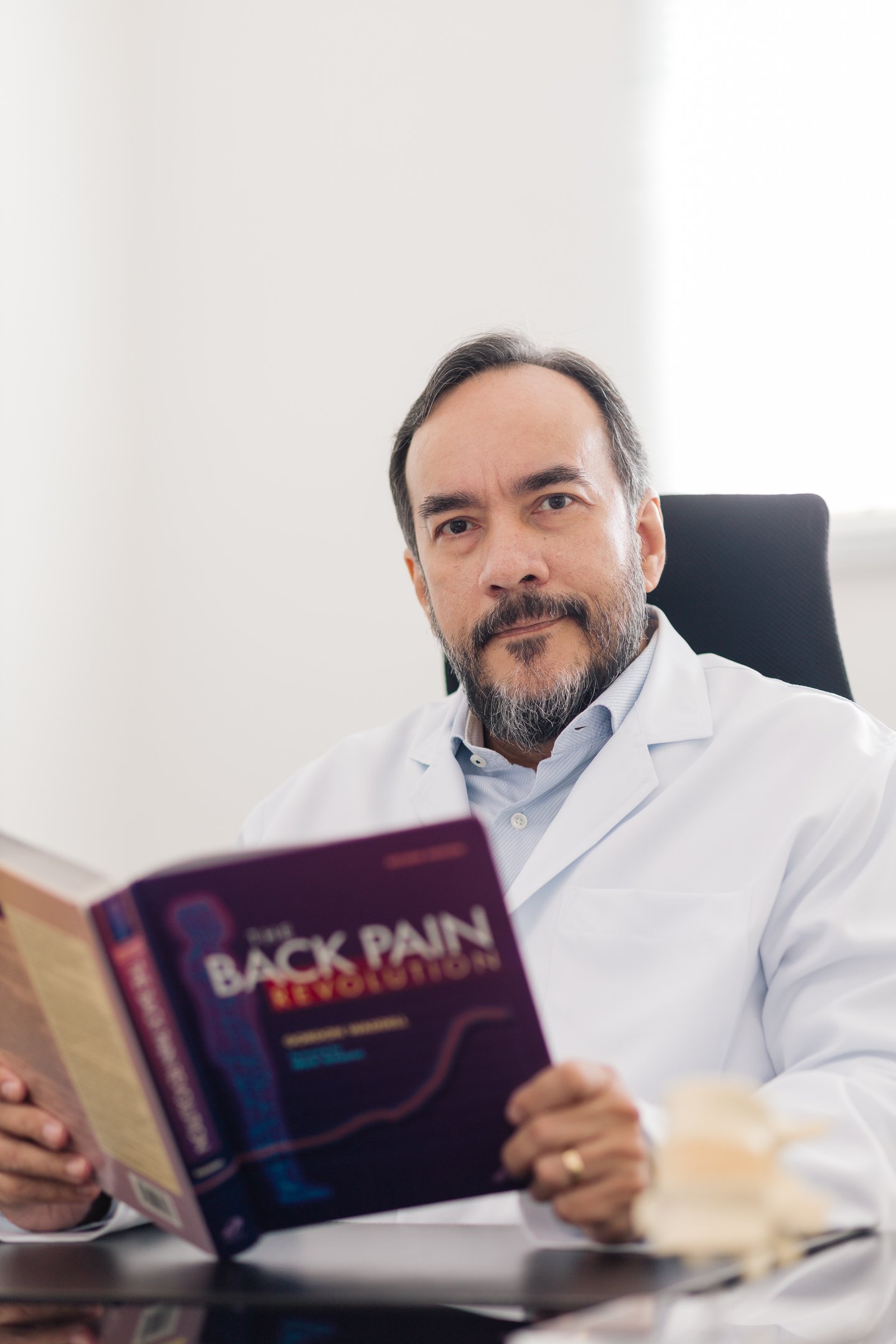 Neurocirurgião Dr. Carlos Moreira especialista em coluna lendo livro sobre dor em consultório.