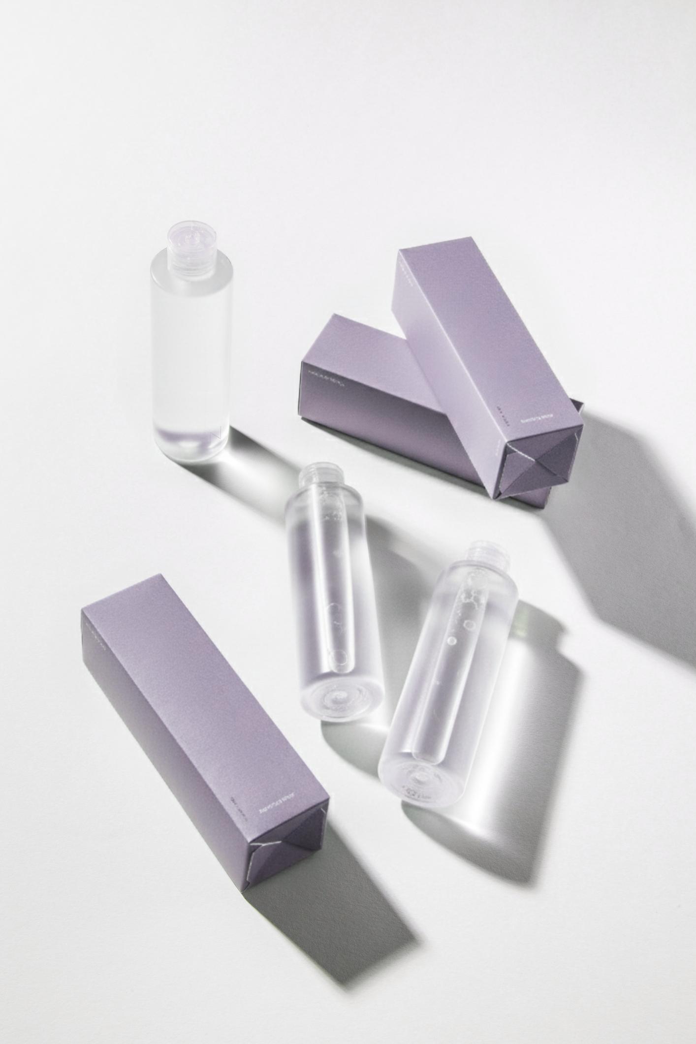 Clear skincare toner bottles with minimalist purple packaging boxes on a white background.