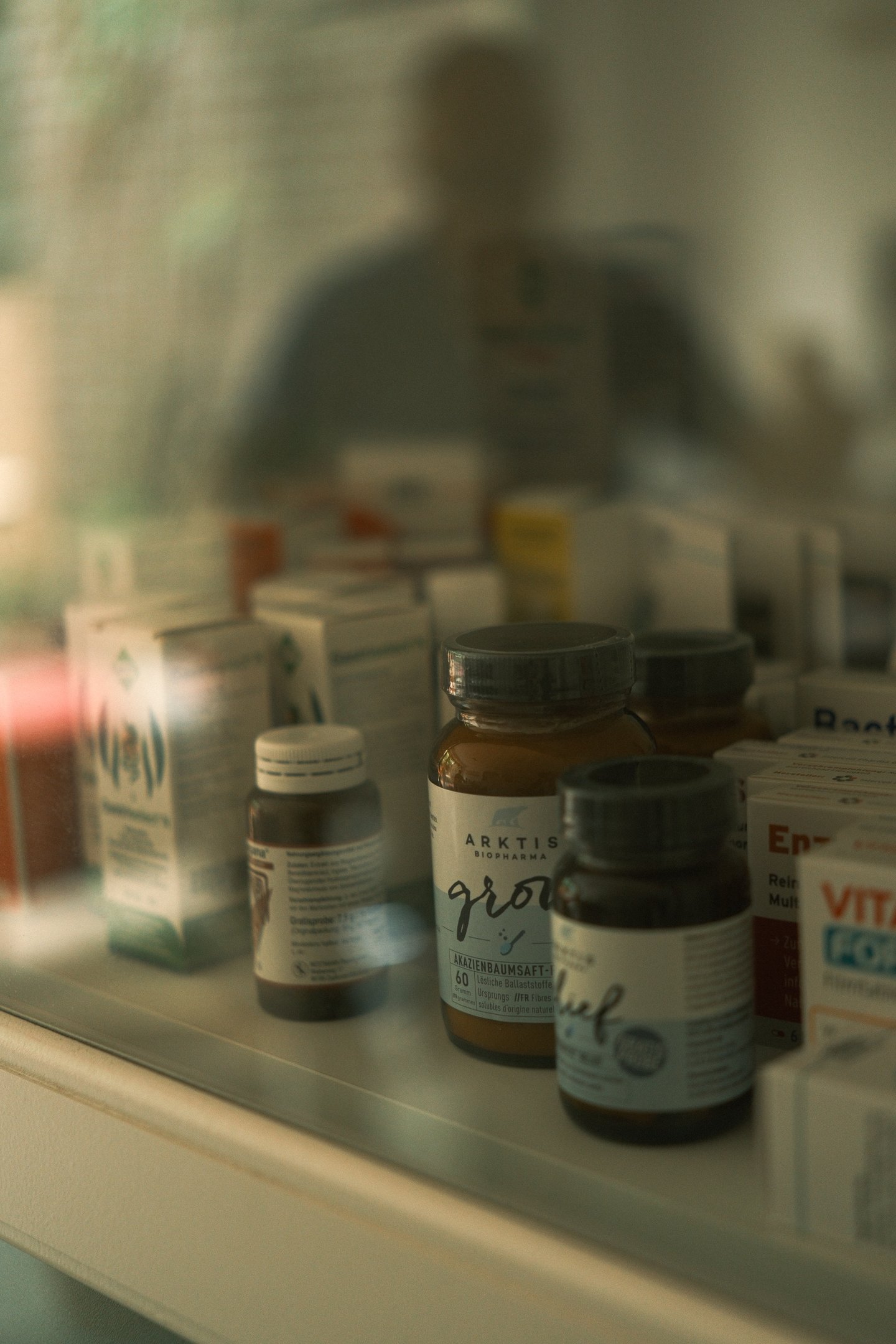 Nahrungsergänzungsmittel im Regal der Heilpraxis Vitalsinn, Spiegelung des Heilpraktikers im Glas