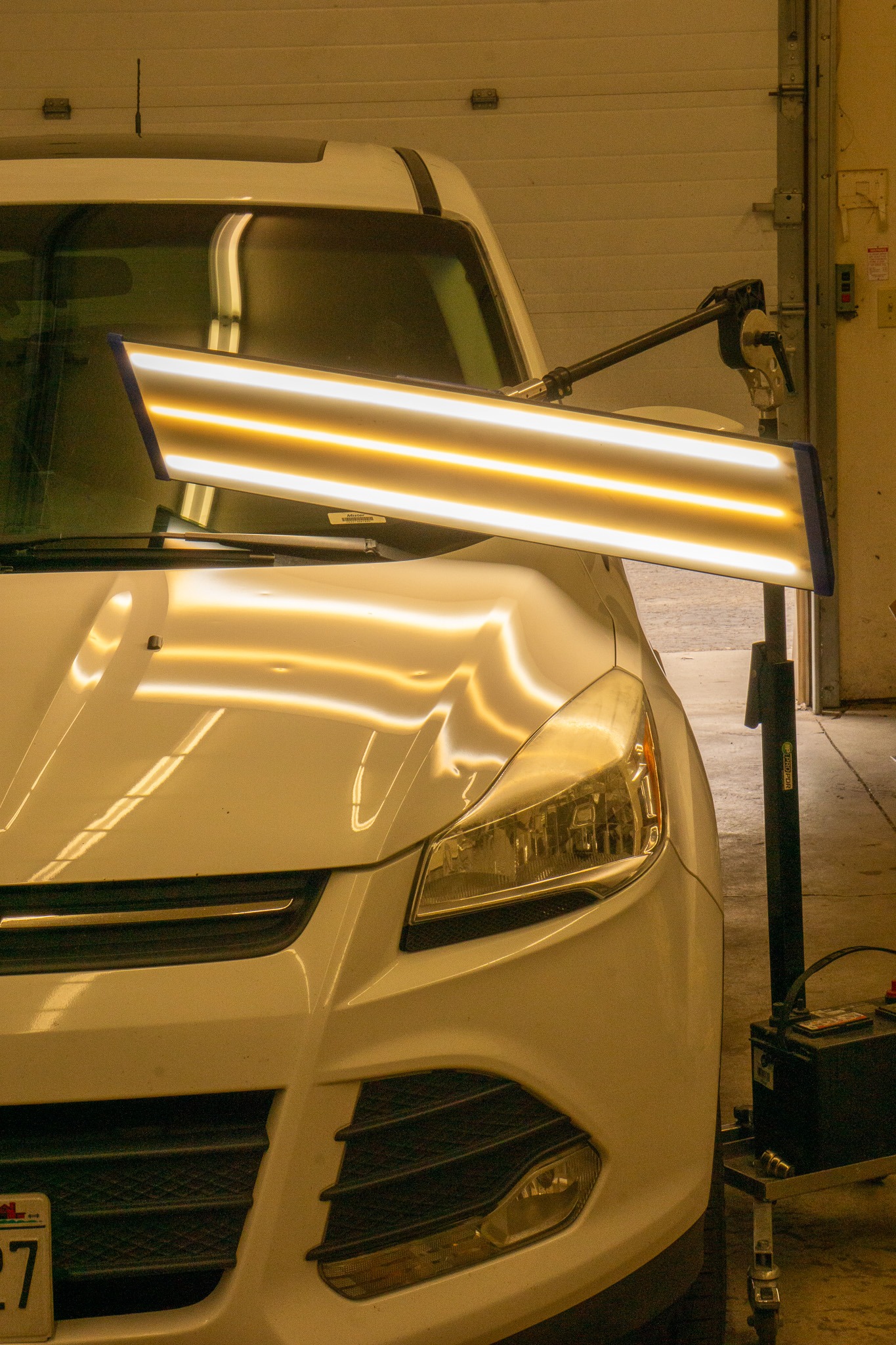 Hail damage on the hood of a white car, shown by the special LED PDR light.