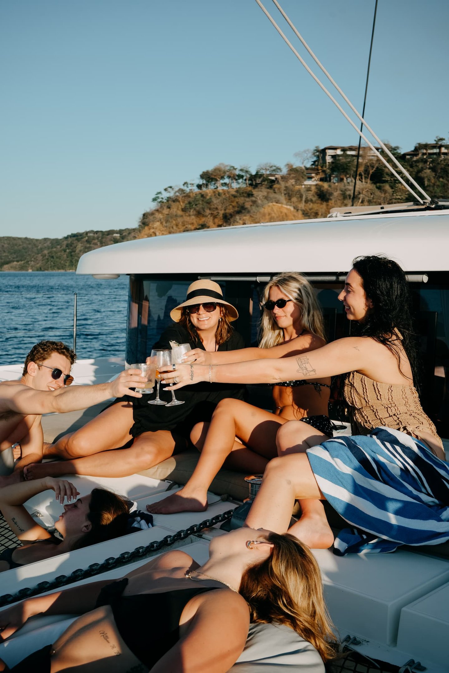 Group of friends toasting with cocktails during sunset cruise on luxury catamaran in Papagayo