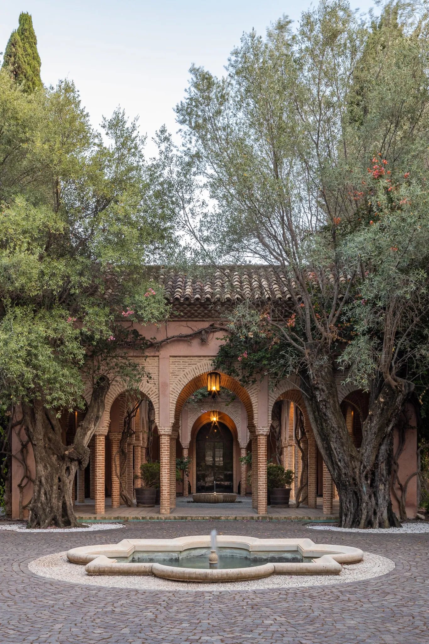 Arched brick courtyard framed by ancient olive trees and central fountain