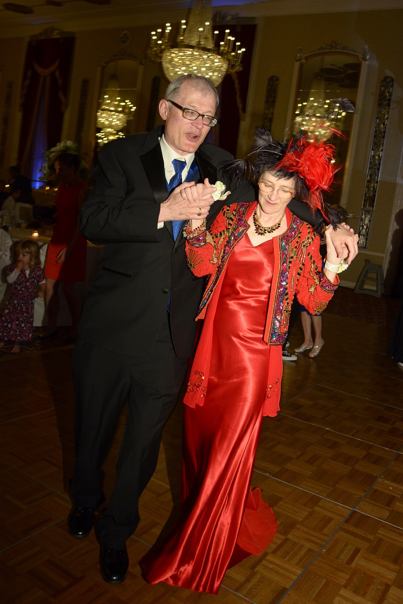 a man in a black suit and blue tie and a woman in a red dress dancing at a dance floor in a wedding