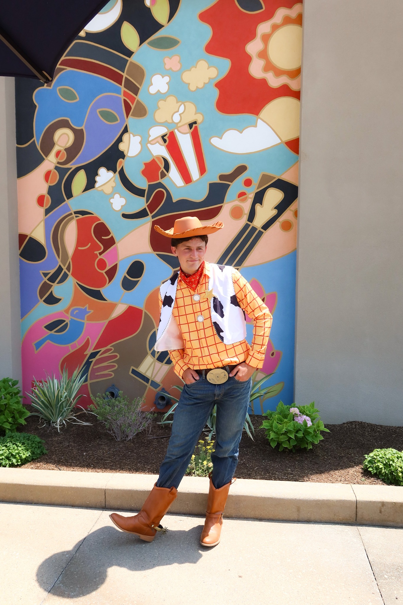 A man wearing a Woody from Toy Story cowboy costume posing in front of a colorful abstract mural.