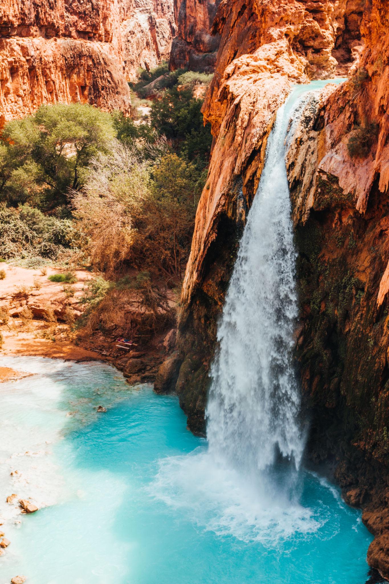 A high-angle view of Havasu Falls cascading into a bright turquoise pool within the Grand Canyon.