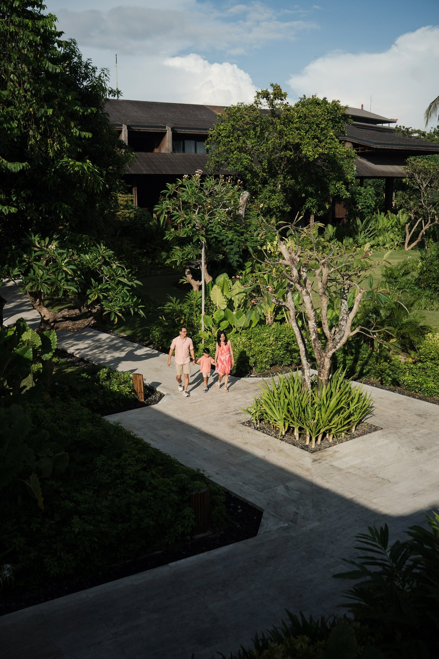 Family walking through tropical garden pathway at The Meru Sanur Bali during a relaxed family photography session