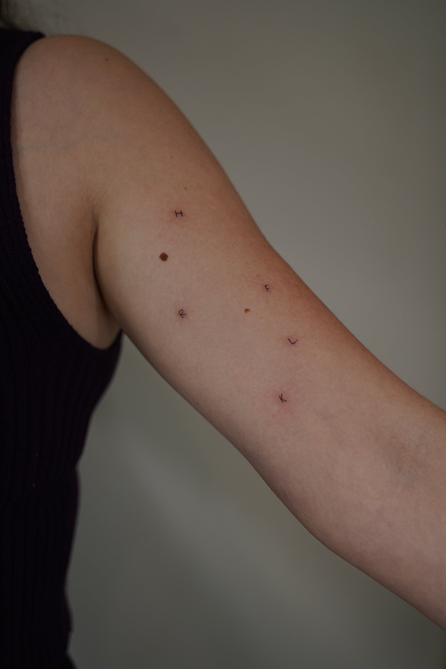 Tatuaje fineline en Madrid de iniciales H F C L K dispersas en trazo fino en el brazo