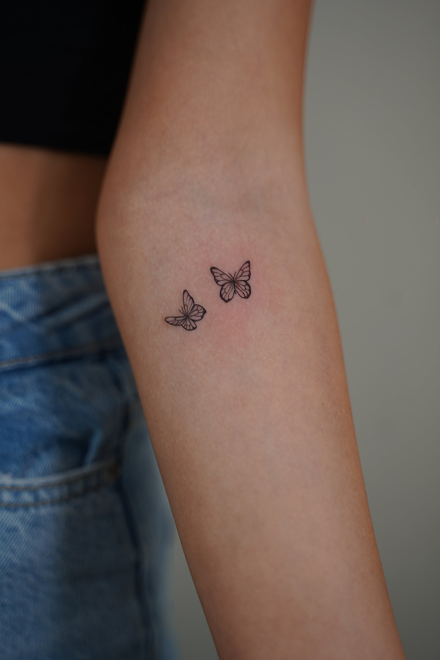 Tatuaje fineline en Madrid de dos mariposas pequeñas en vuelo con trazo delicado en el antebrazo