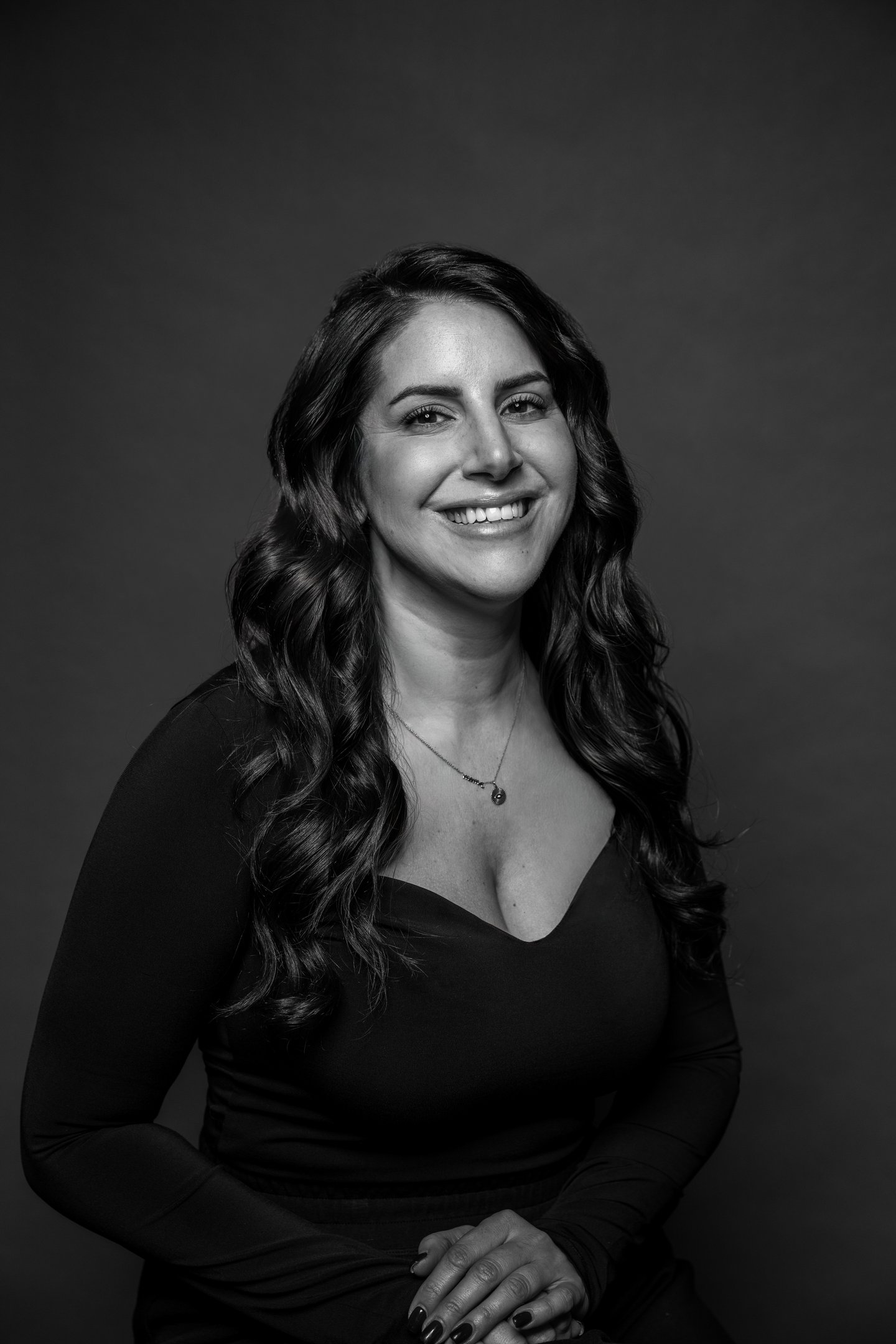 Portrait professionnel en noir et blanc d’une femme souriante aux cheveux longs ondulés