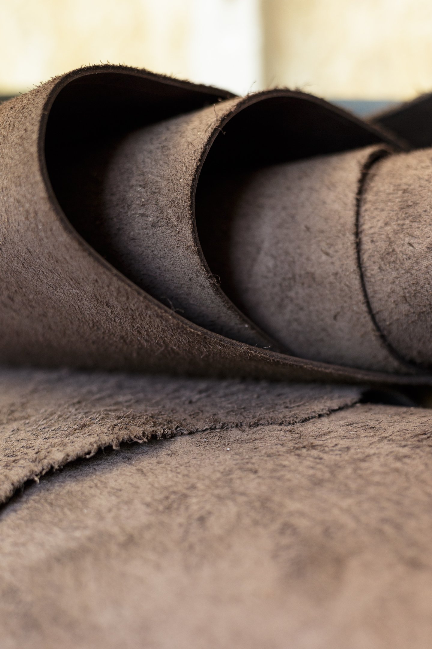 Close-up of high-quality brown suede leather fabric roll with a soft, napped texture for upholstery or crafts.