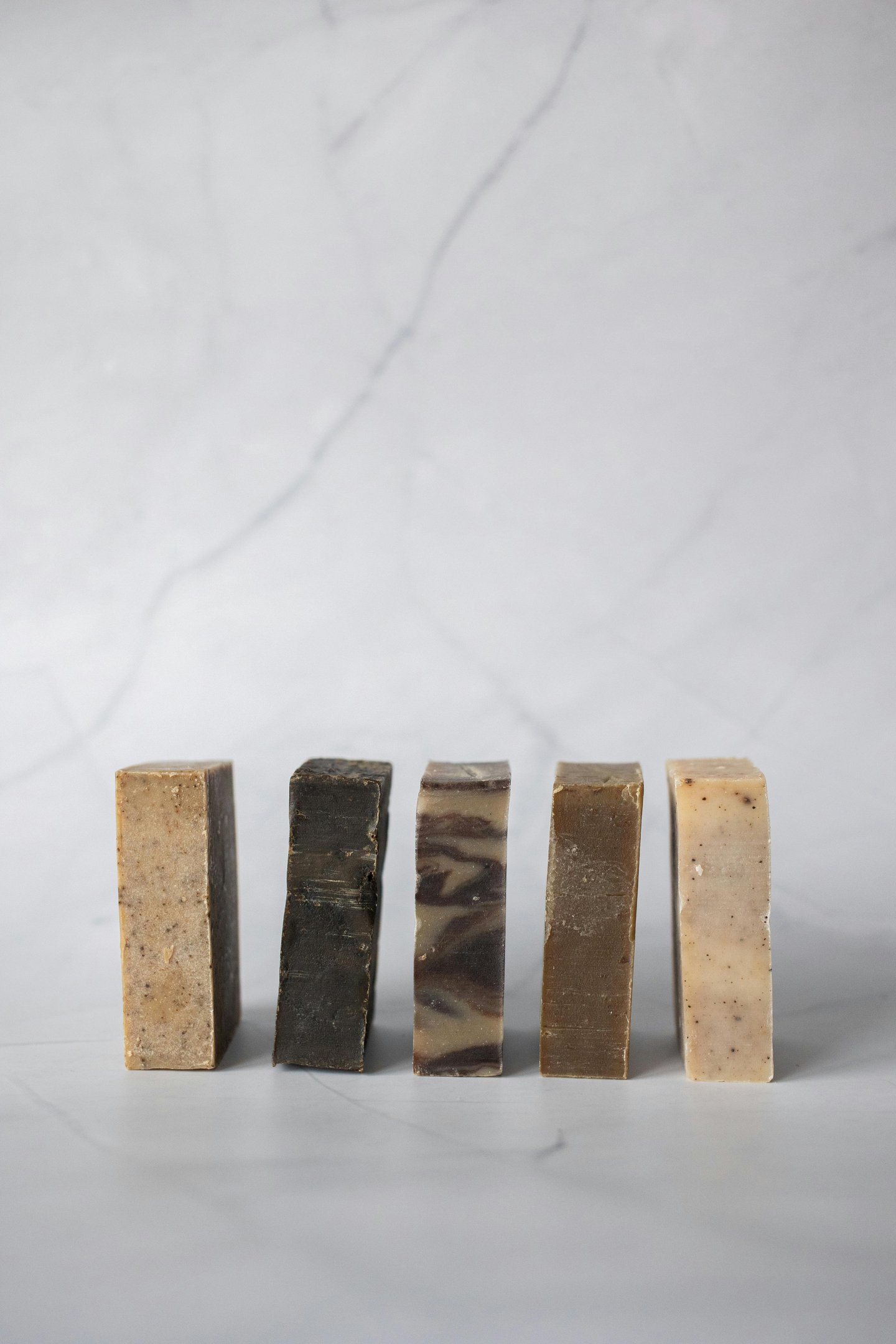 A row of five assorted natural handmade soap bars standing upright on a white marble surface.