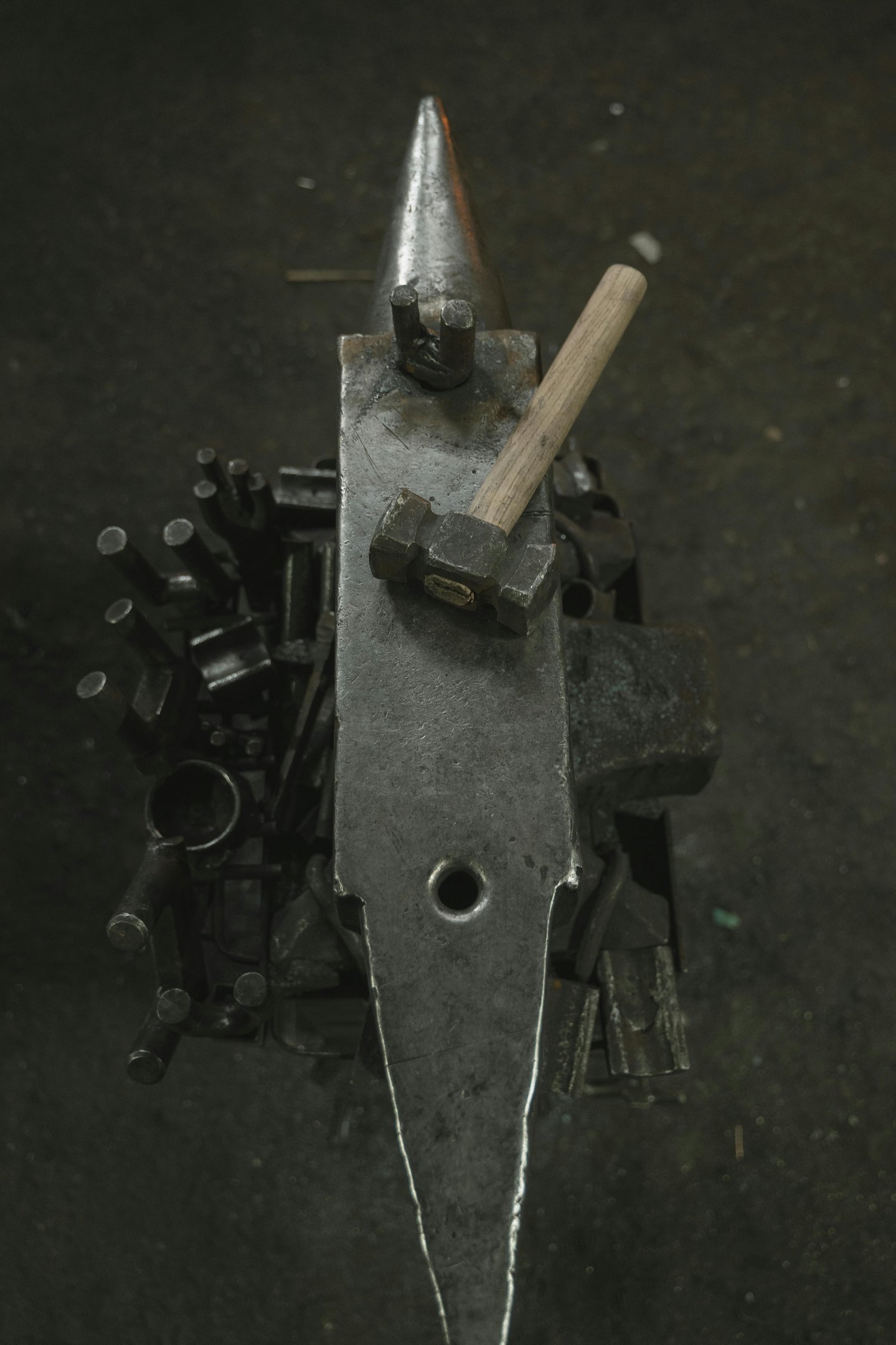 Overhead view of a traditional metal forging anvil and blacksmith hammer in a dark workshop.