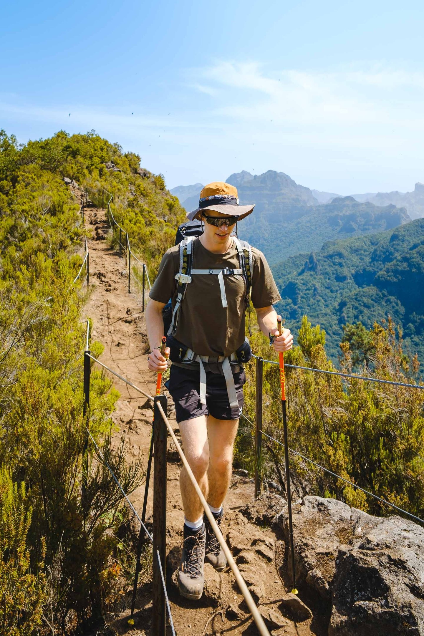 Wanderer mit Rucksack und Stöcken auf einem schmalen Bergpfad. Outdoor-Foto von Joel Pingel.