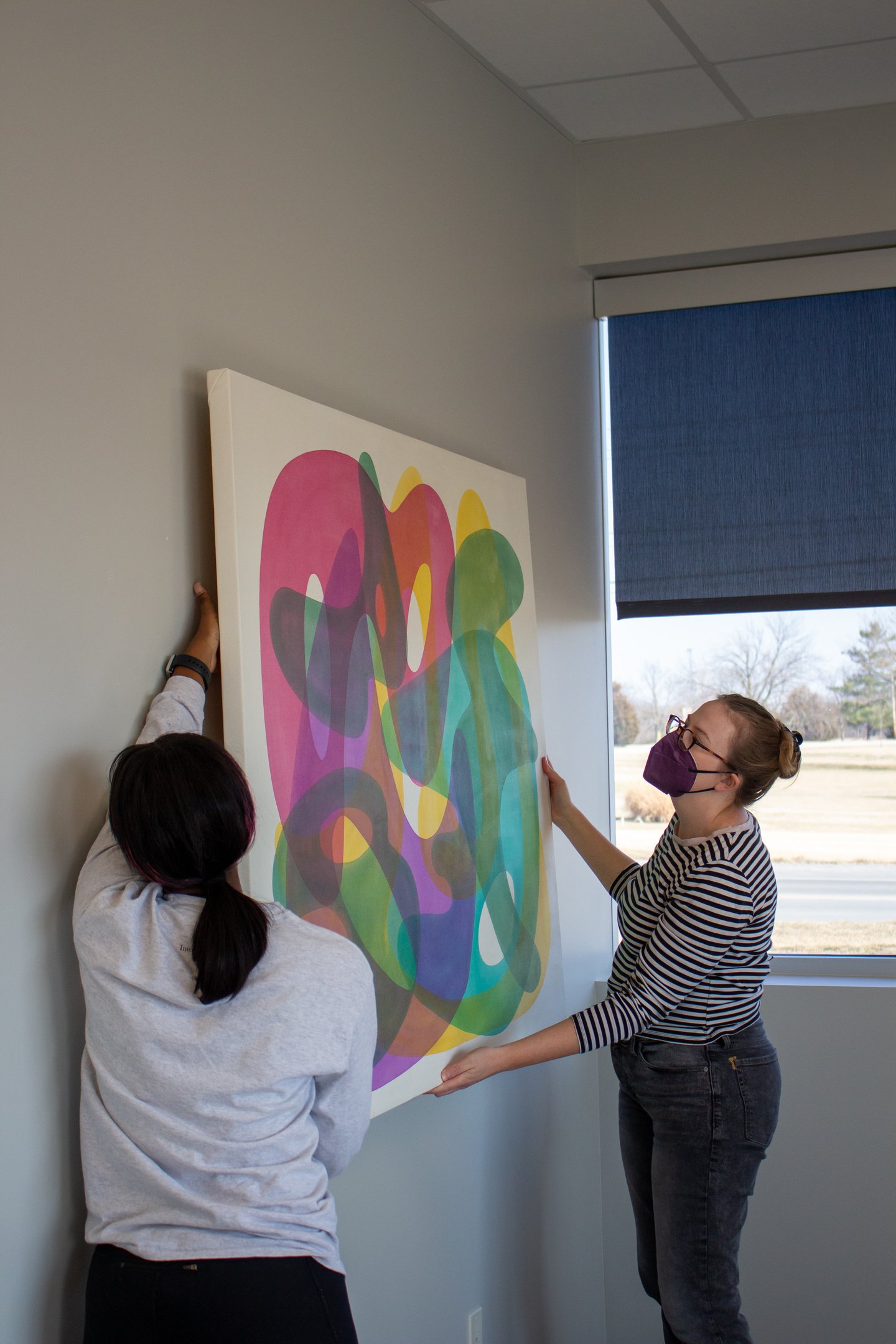 Two individuals hanging a colorful painting on one of our walls.