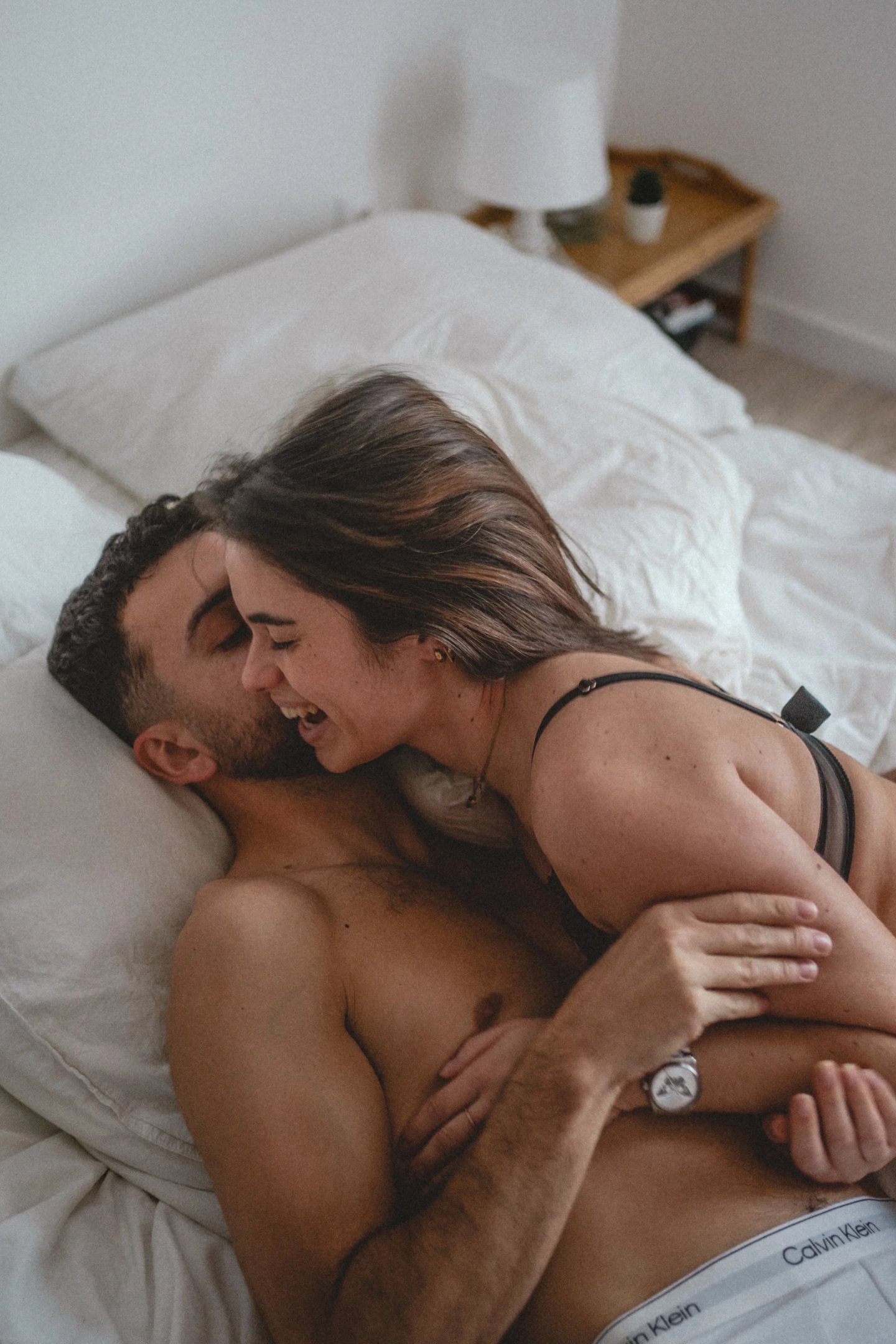 Couple riant, allongé dans un lit lors d’une séance photo de couple intimiste à Rennes.