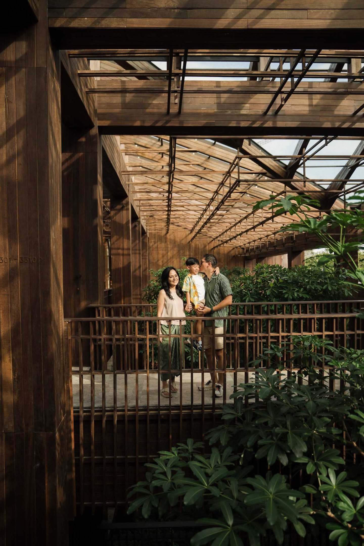 Family standing on a wooden bridge surrounded by tropical greenery during a family photography session at The Meru Sanur Bali