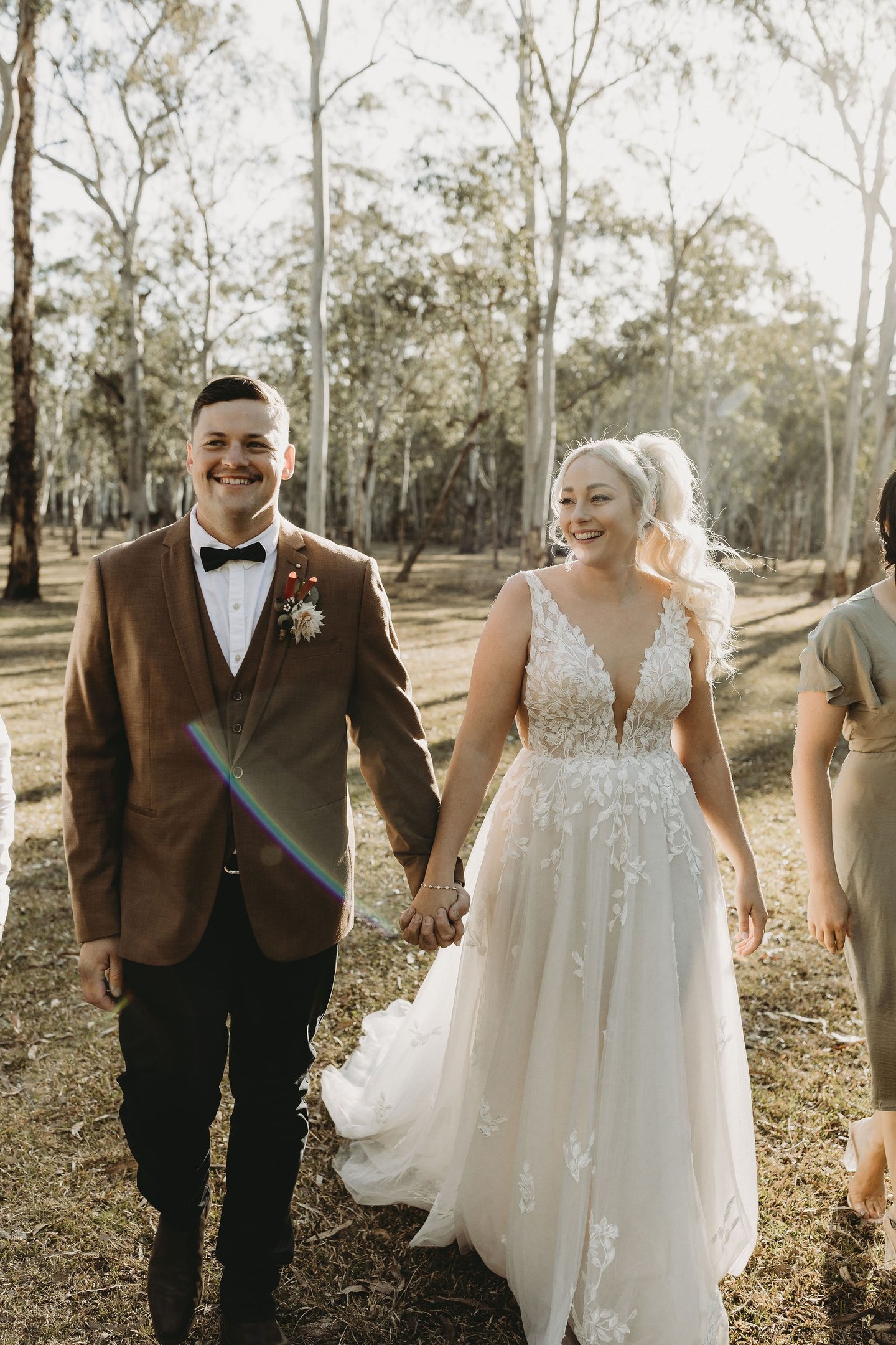 a bride and groom walking down a path in a wooded area