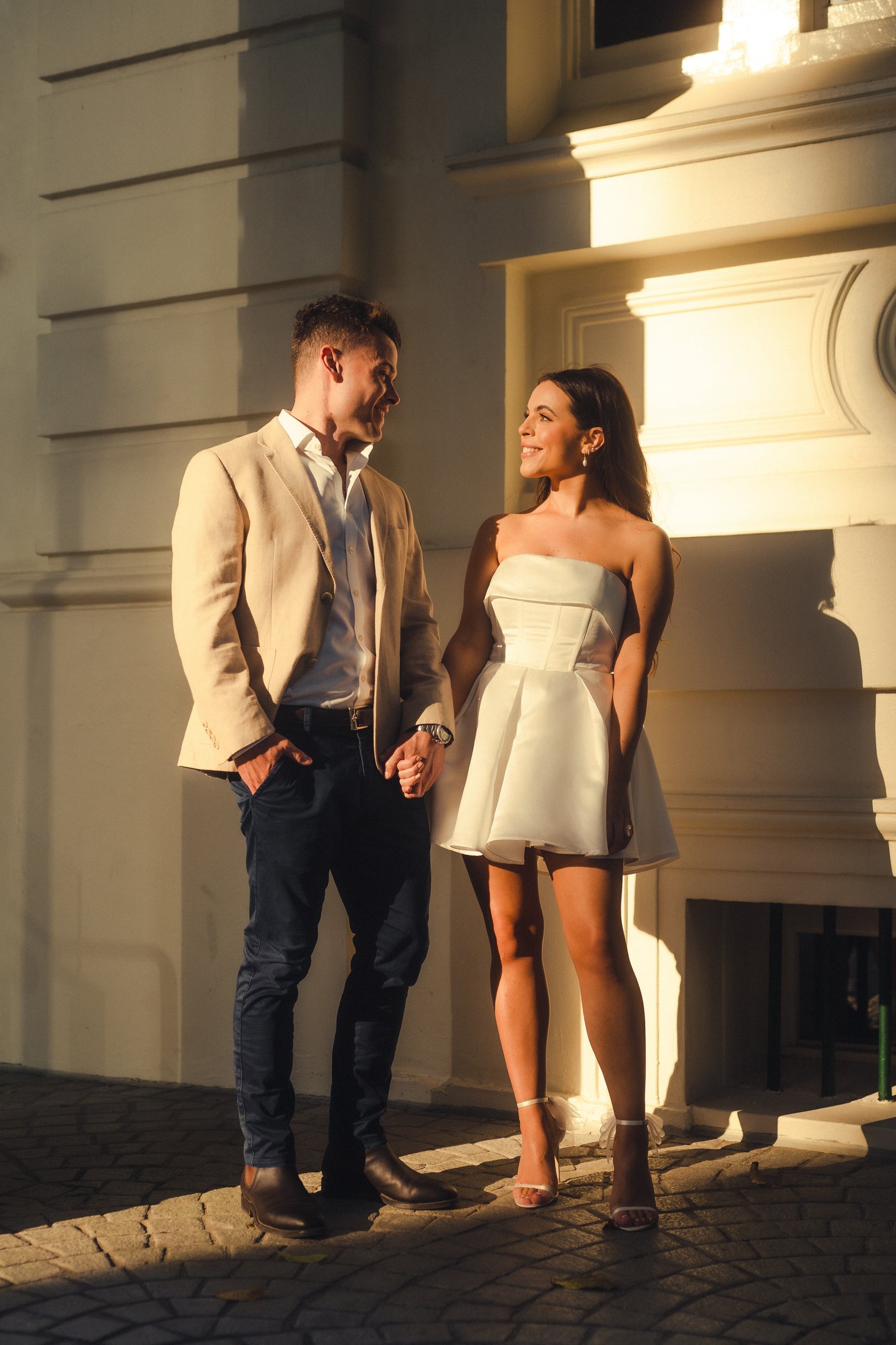 a man and woman holding hands and walking down a cobblestone