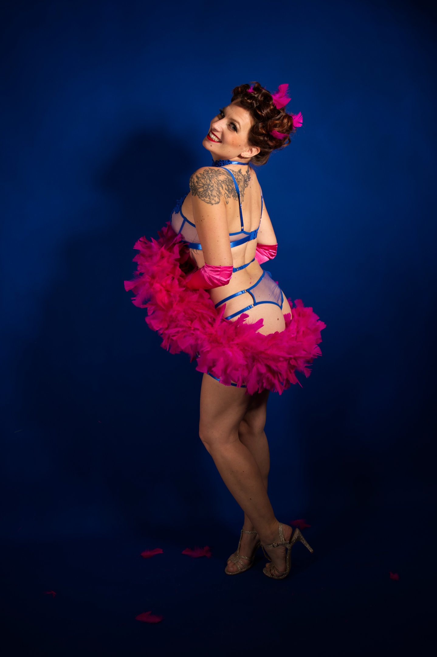 Pin up joyeuse en lingerie bleue avec un boa en plumes rose, qui sourie.