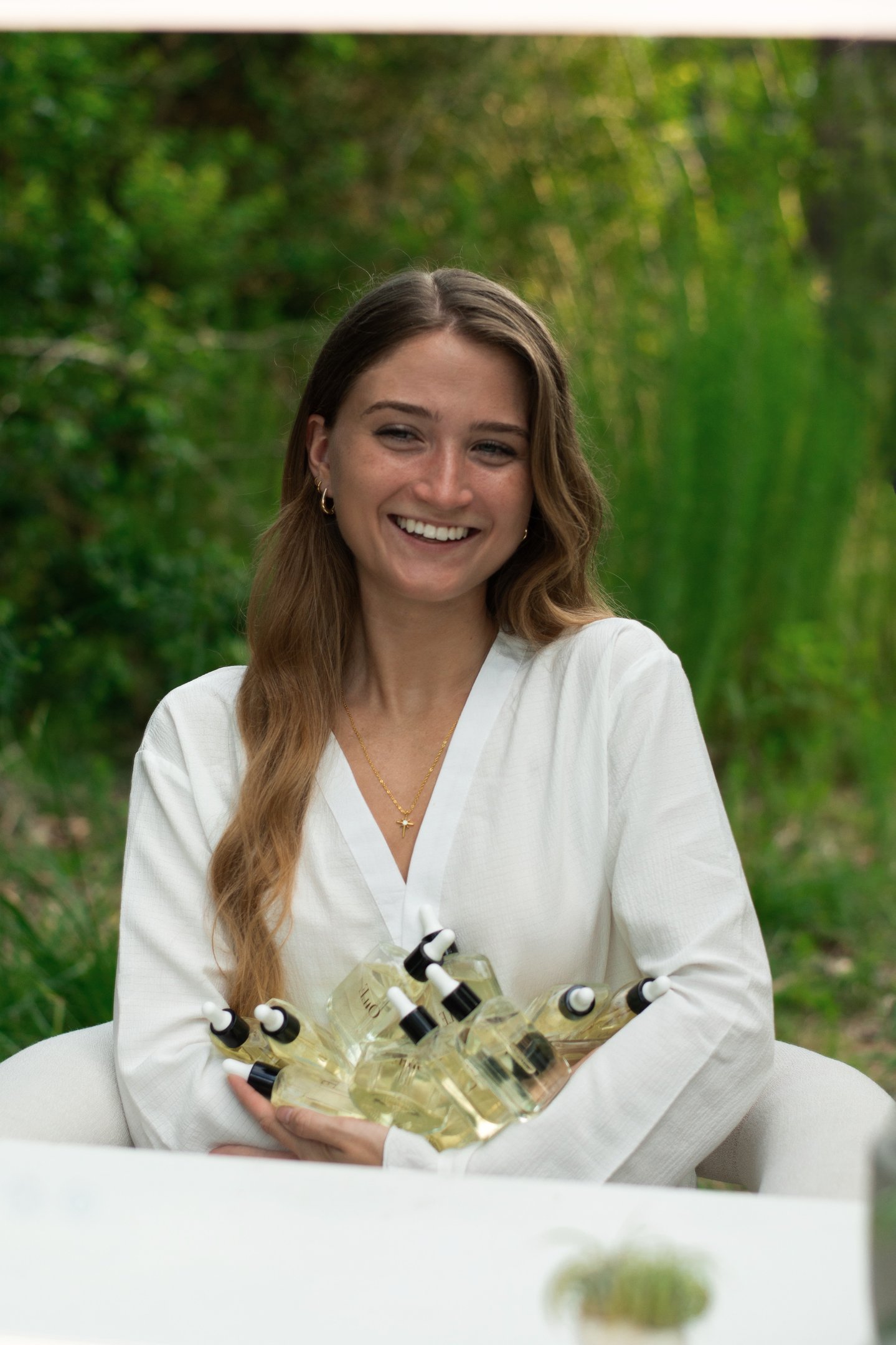 Smiling woman holding a bundle of natural glass dropper bottles for organic skincare products.