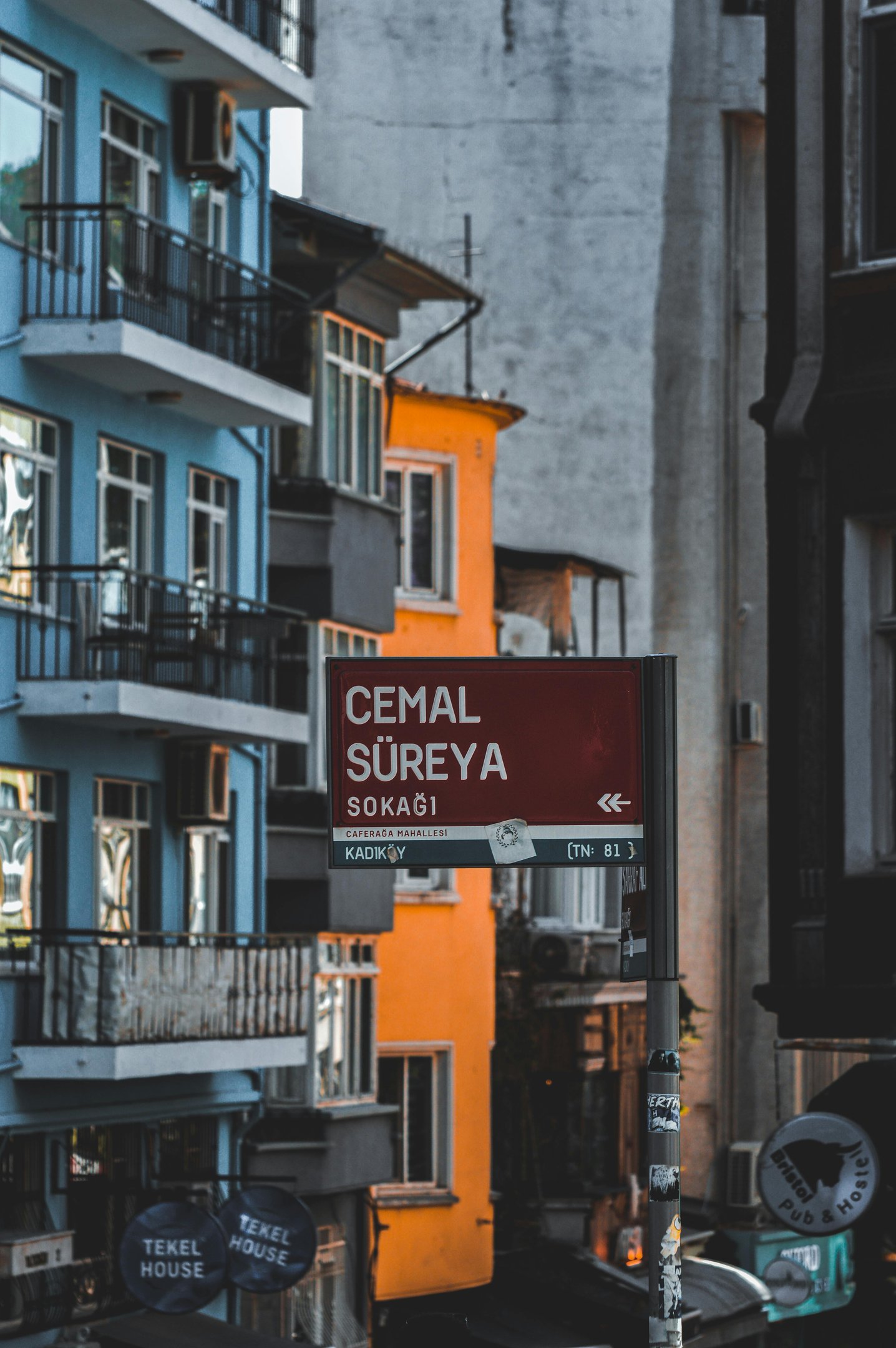 Red Cemal Süreya street sign in the Kadıköy district of Istanbul featuring colorful blue and orange buildings.
