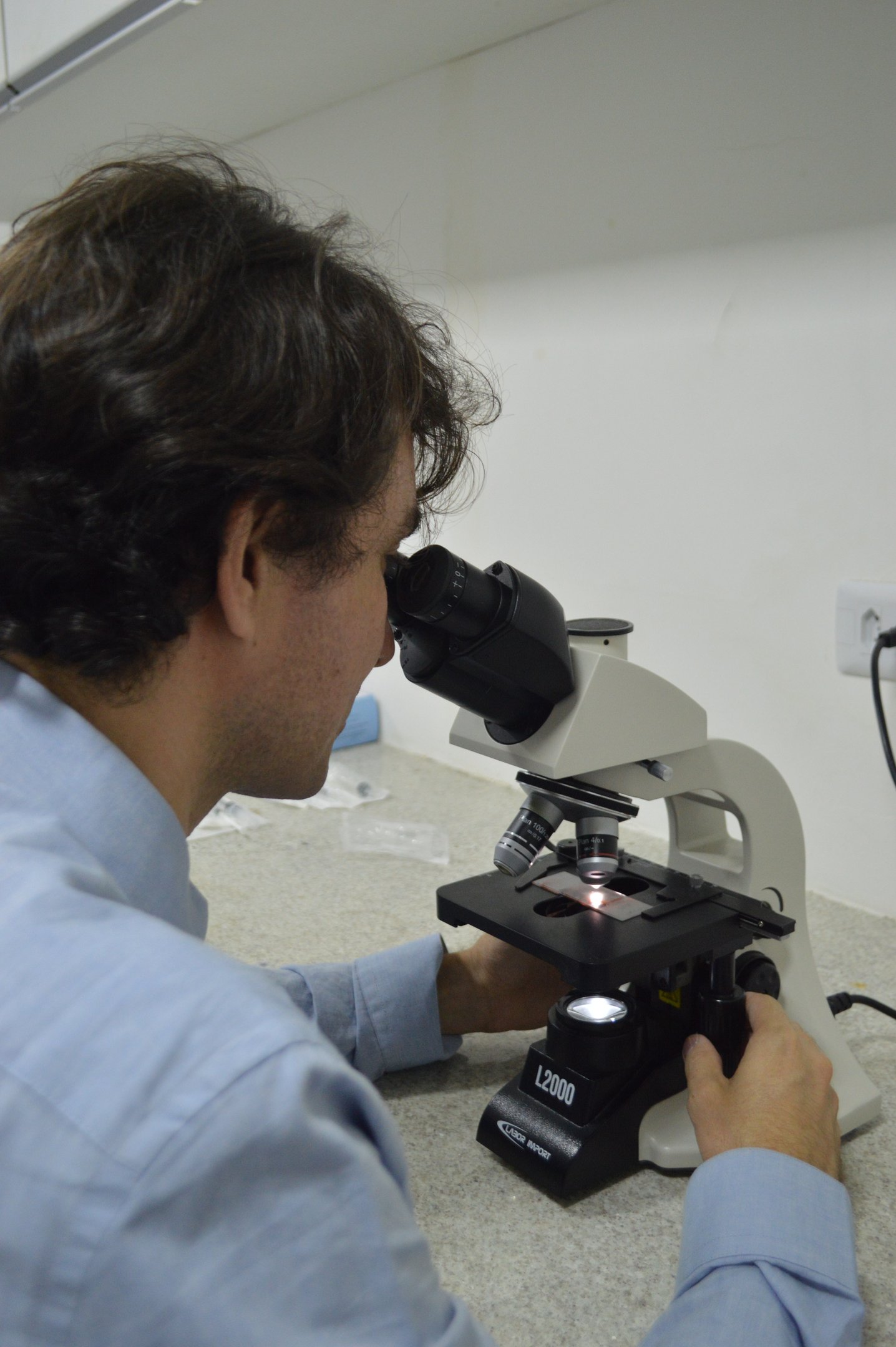 Citologista clínico analisando amostra em microscópio.