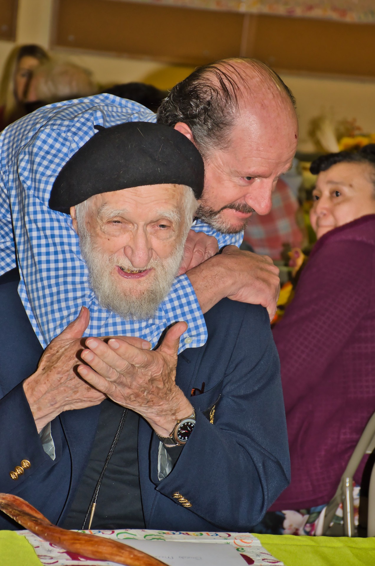 a man in a blue jacket is holding an old man's shoulder 