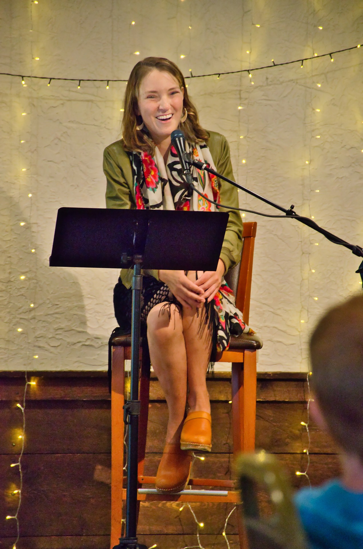 a woman sitting in a chair with a microphone smiling at the audience