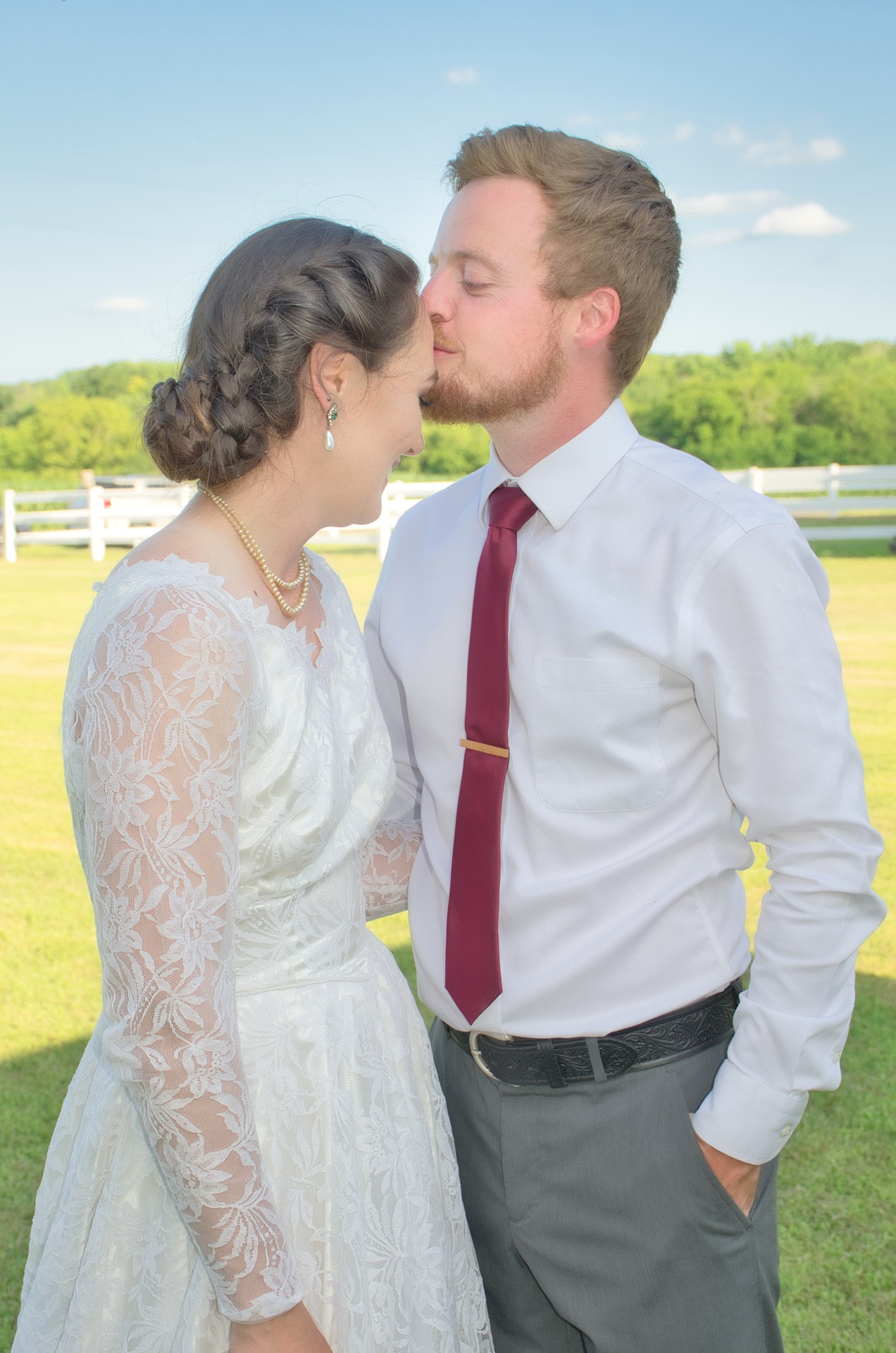 a groom kissing his bride's forehead in a farmland