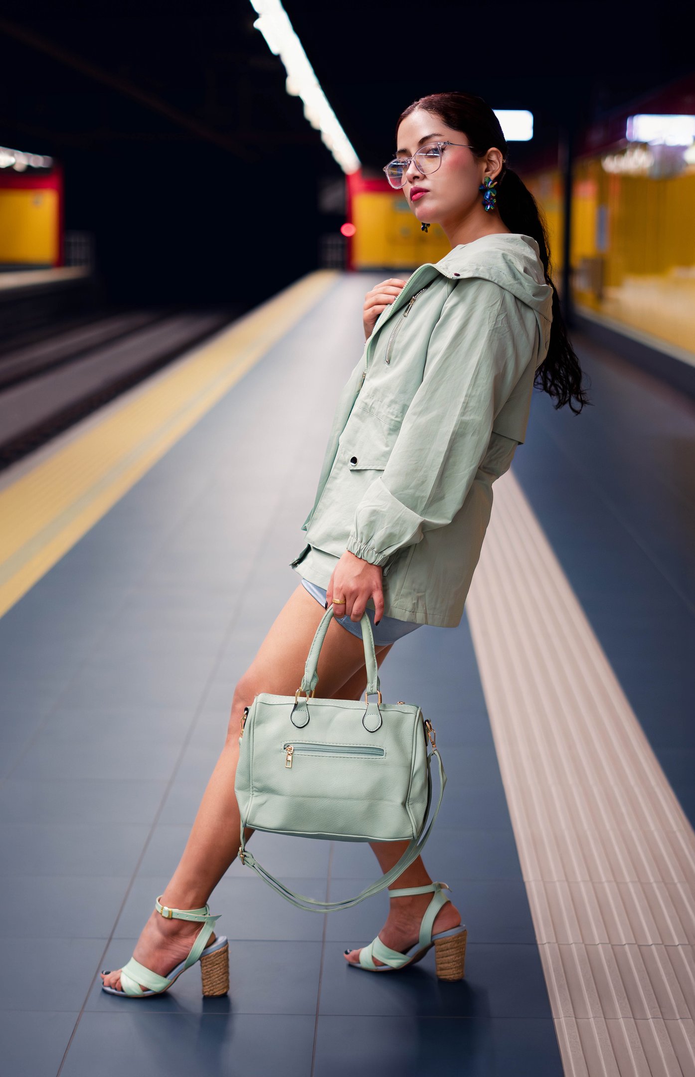a woman in a green coat and heels is holding a purse