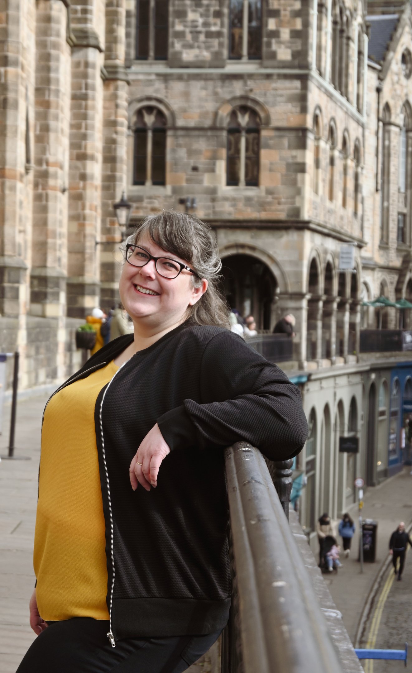 Laura is leaning against a railing and smiling at the camera