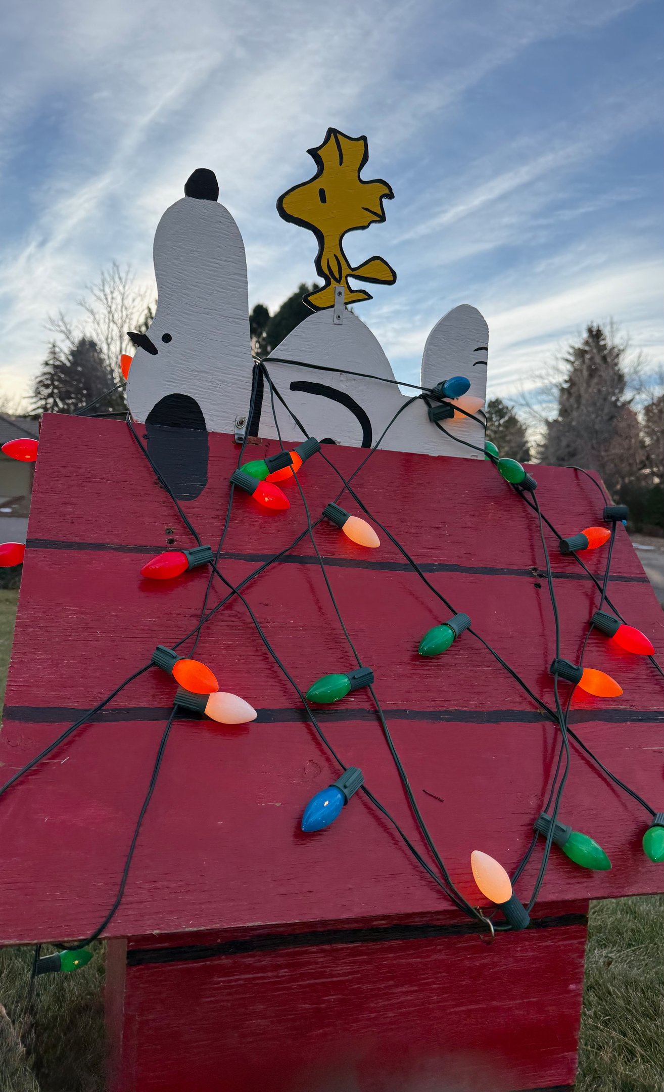 Lawn decoration of Snoopy and Woodstock on a red dog house wrapped in Christmas lights