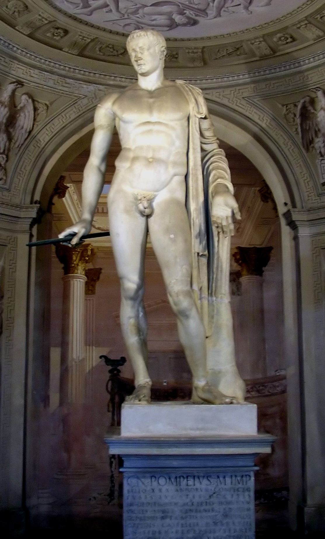 Full-length ancient Roman marble statue of a heroic nude male figure standing in a classic pose inside a vaulted alcove.