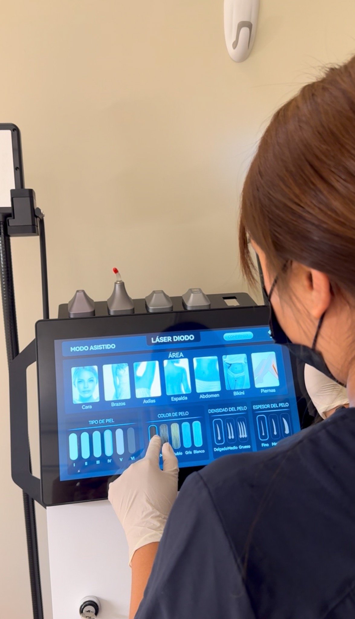 Esthetician using a professional diode laser hair removal machine touchscreen to select treatment settings.