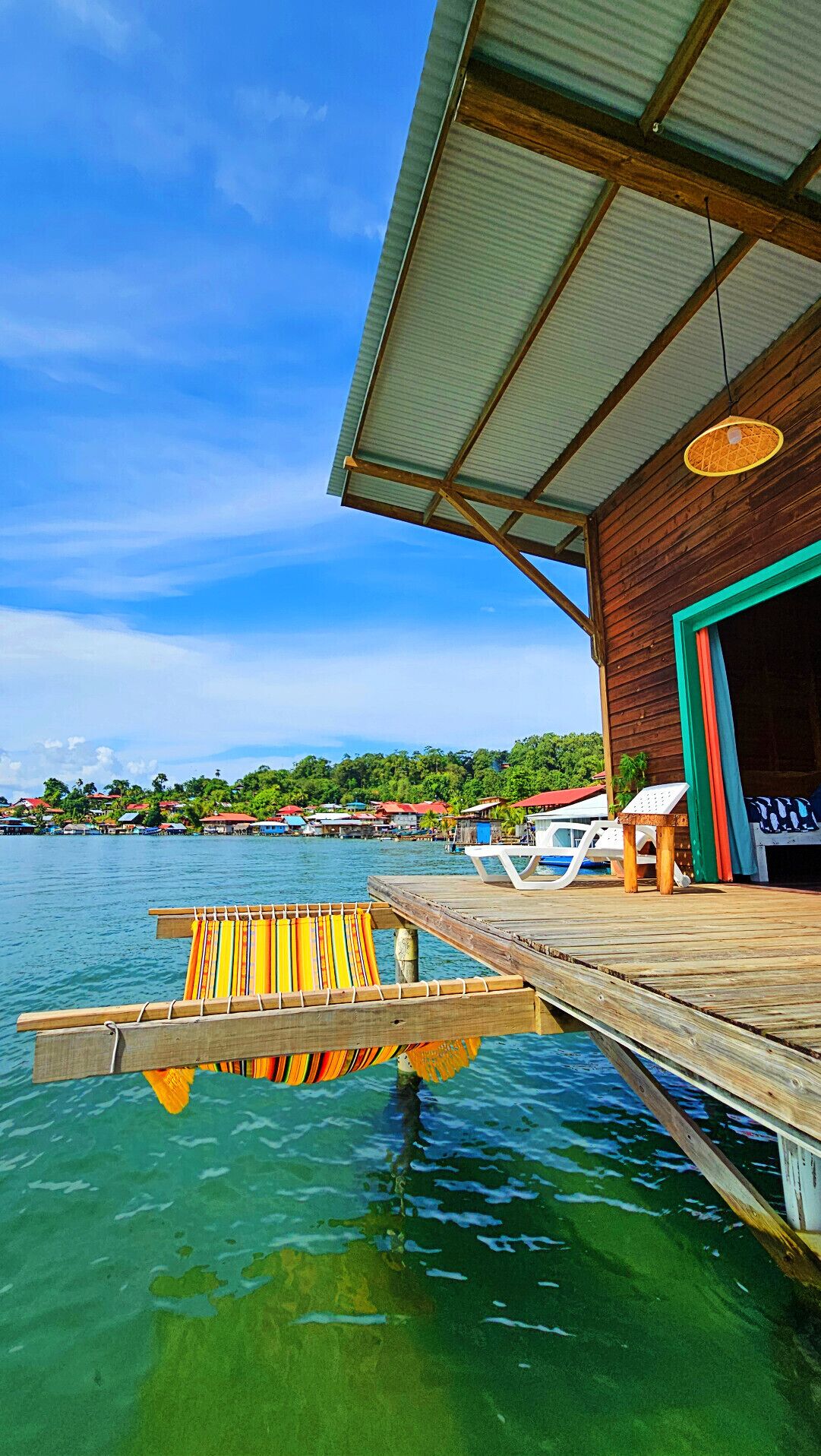 Tropical overwater bungalow with a wooden deck and hammock overlooking turquoise ocean water.