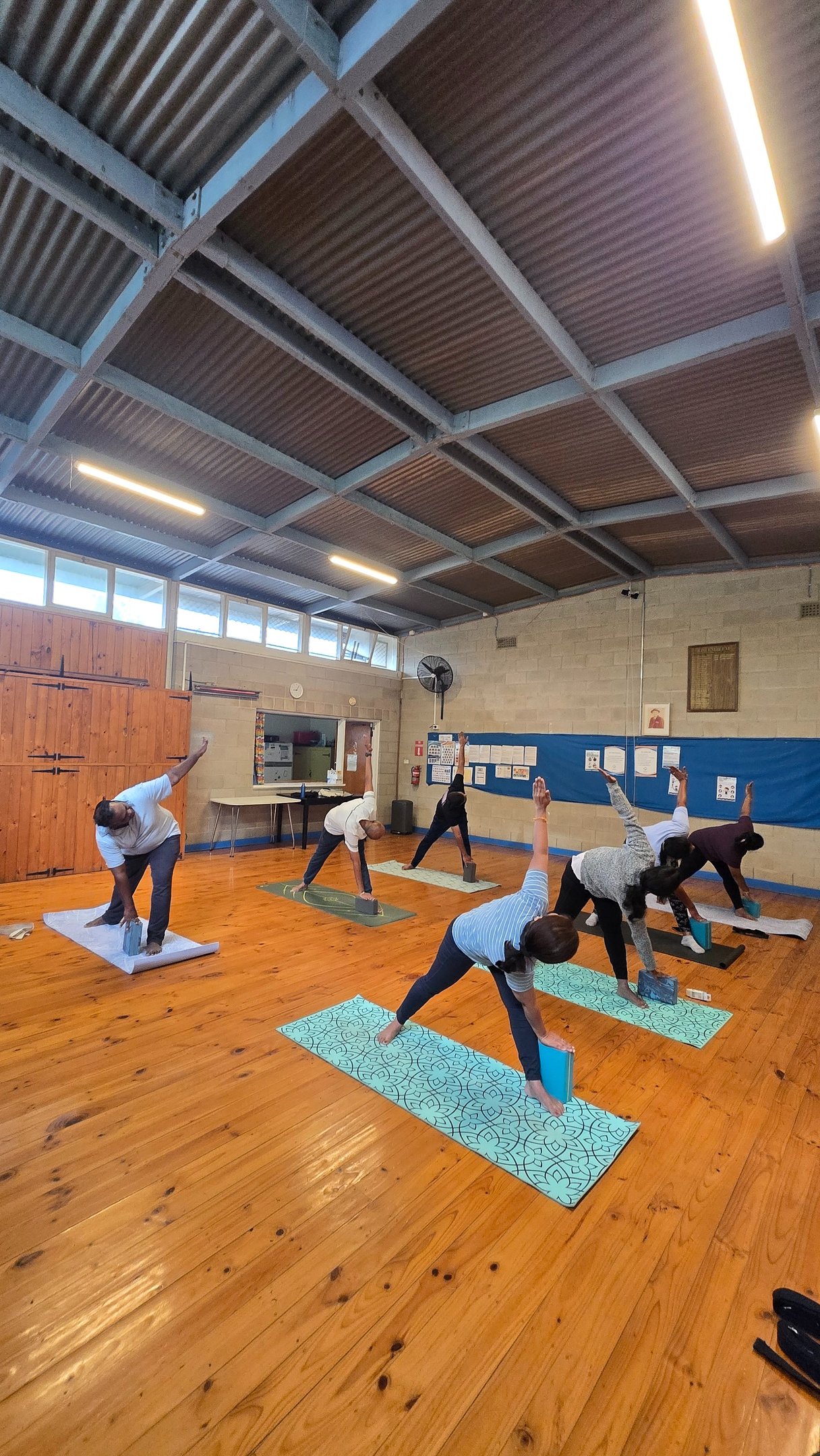 Group yoga class practicing triangle pose with foam blocks on mats in a studio.