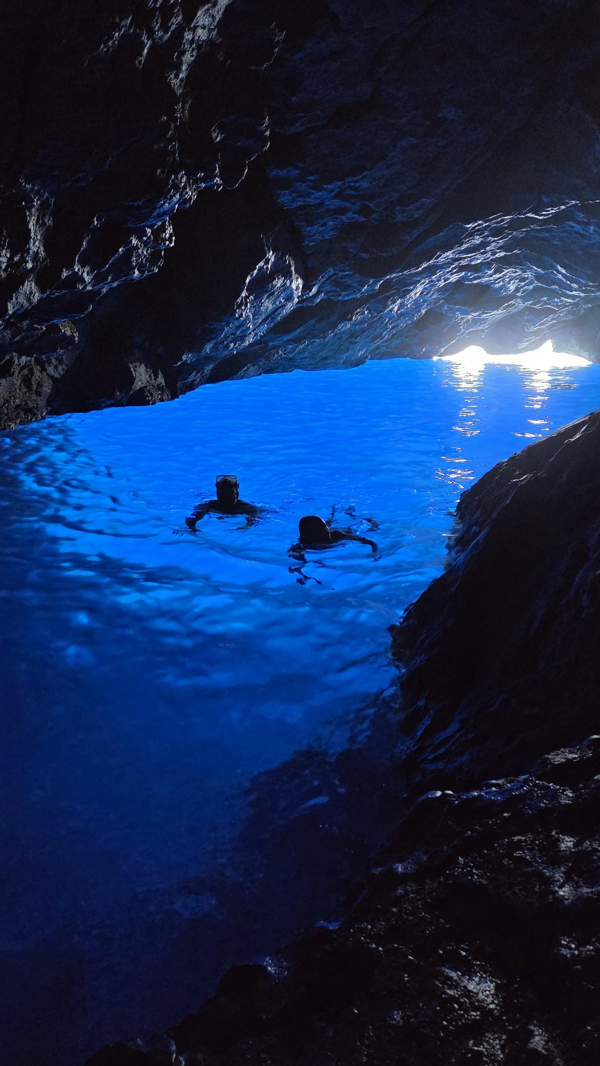 Couple nageant dans une eau bleue azur a l'intérieur d'une grotte marine.