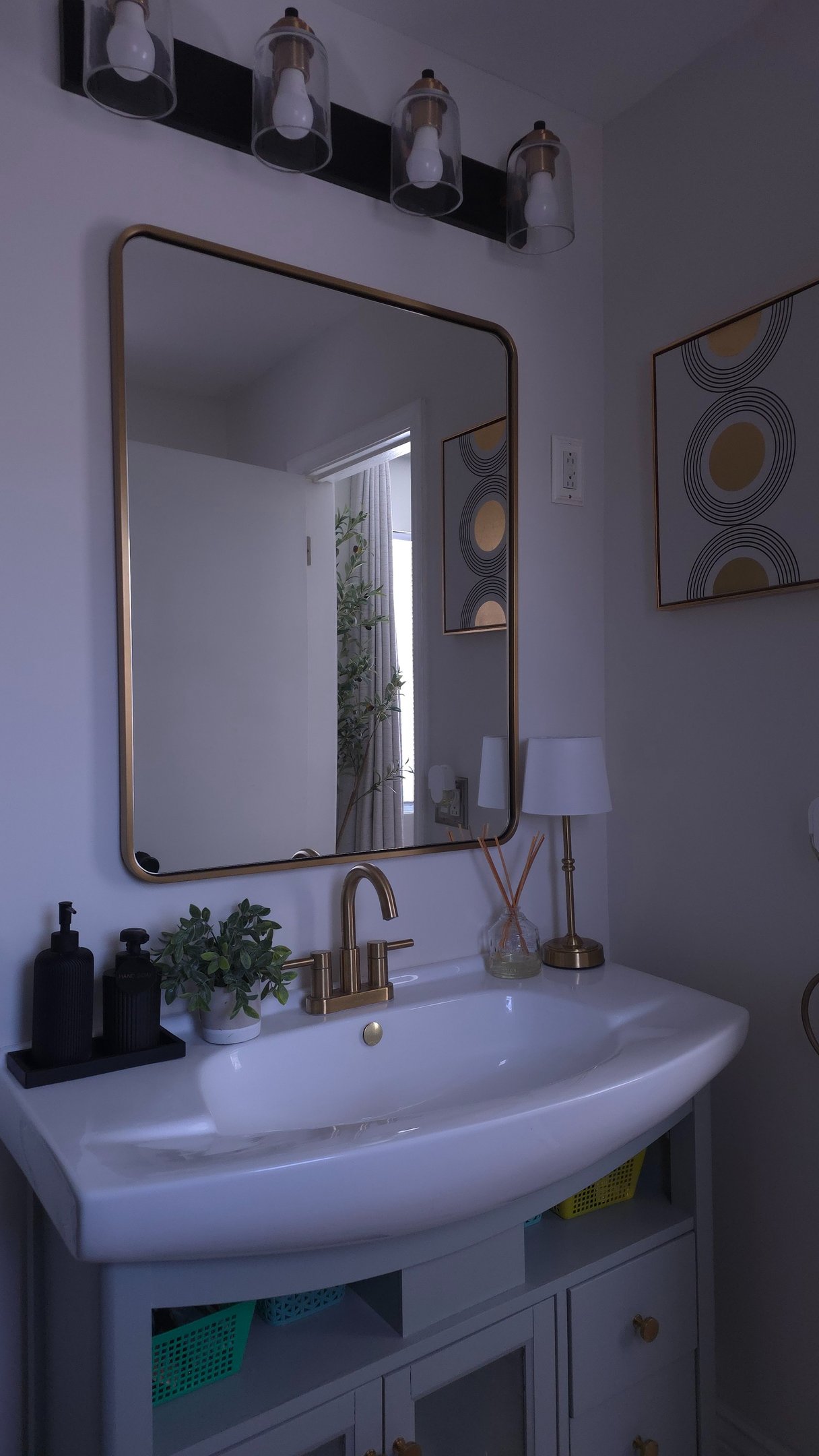 Modern bathroom vanity with gold framed mirror, brass faucet, and white pedestal sink.