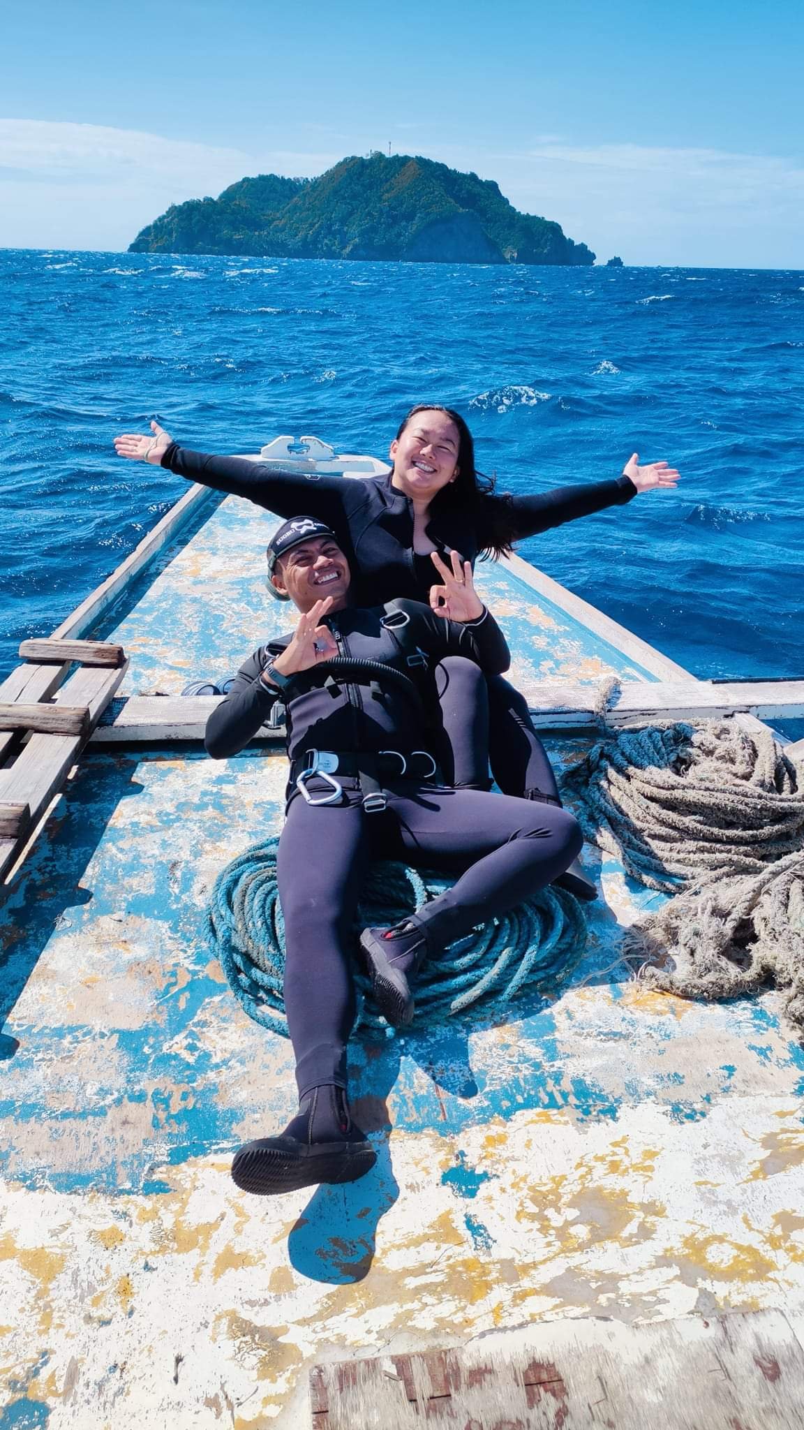 Sugbu Diver in a wetsuit with full scuba gear lying at the tip of the boat, raising her hands wide
