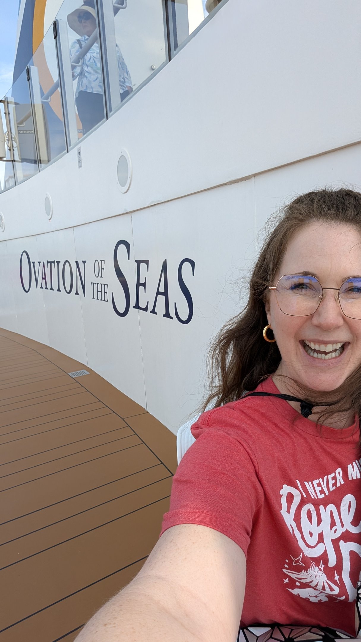 A woman smiling by the side of a Royal Caribbean ship that says Ovation of the Seas