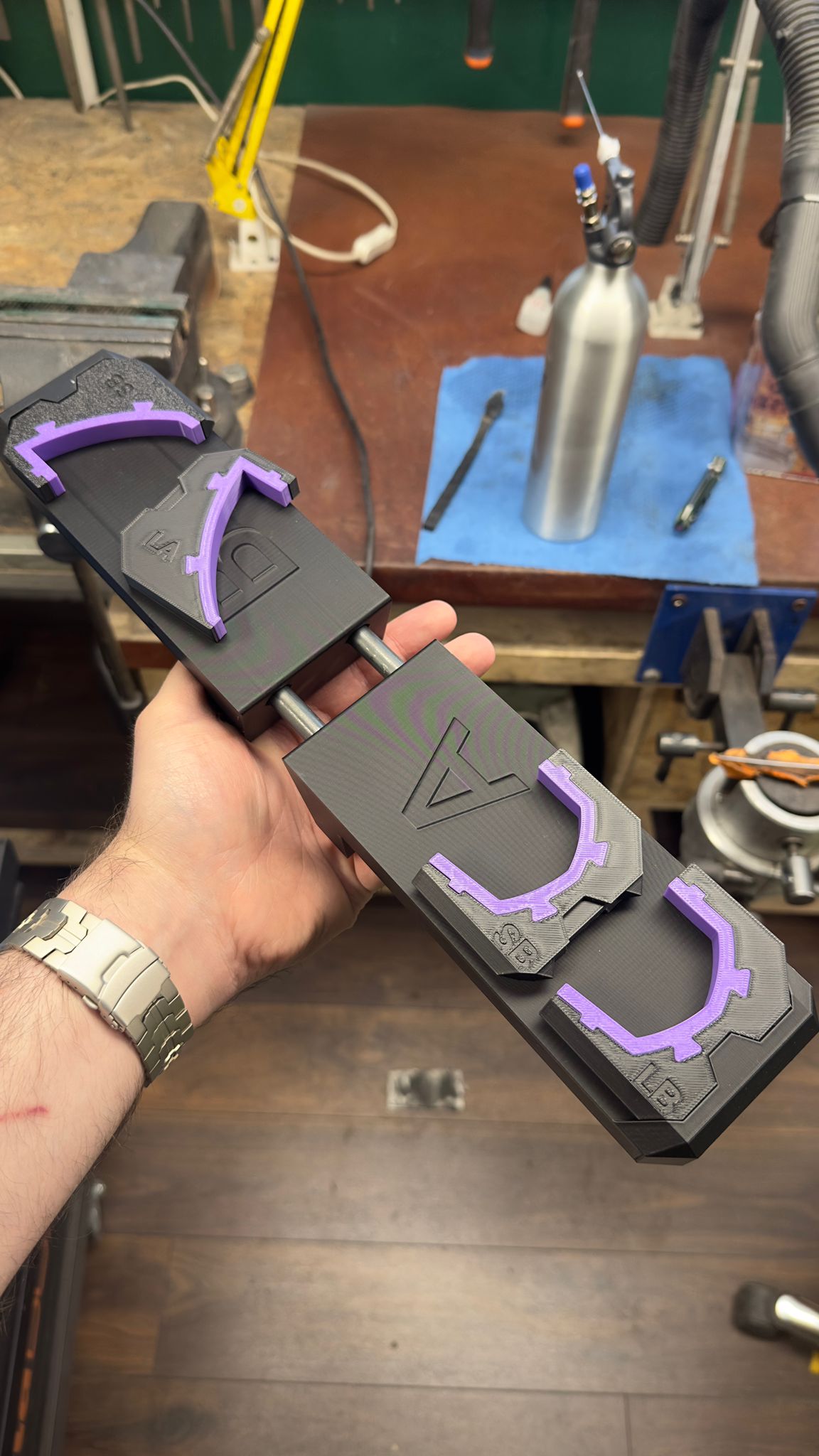 A hand holding a 3D printed mechanical assembly with black and purple plastic components in a workshop.