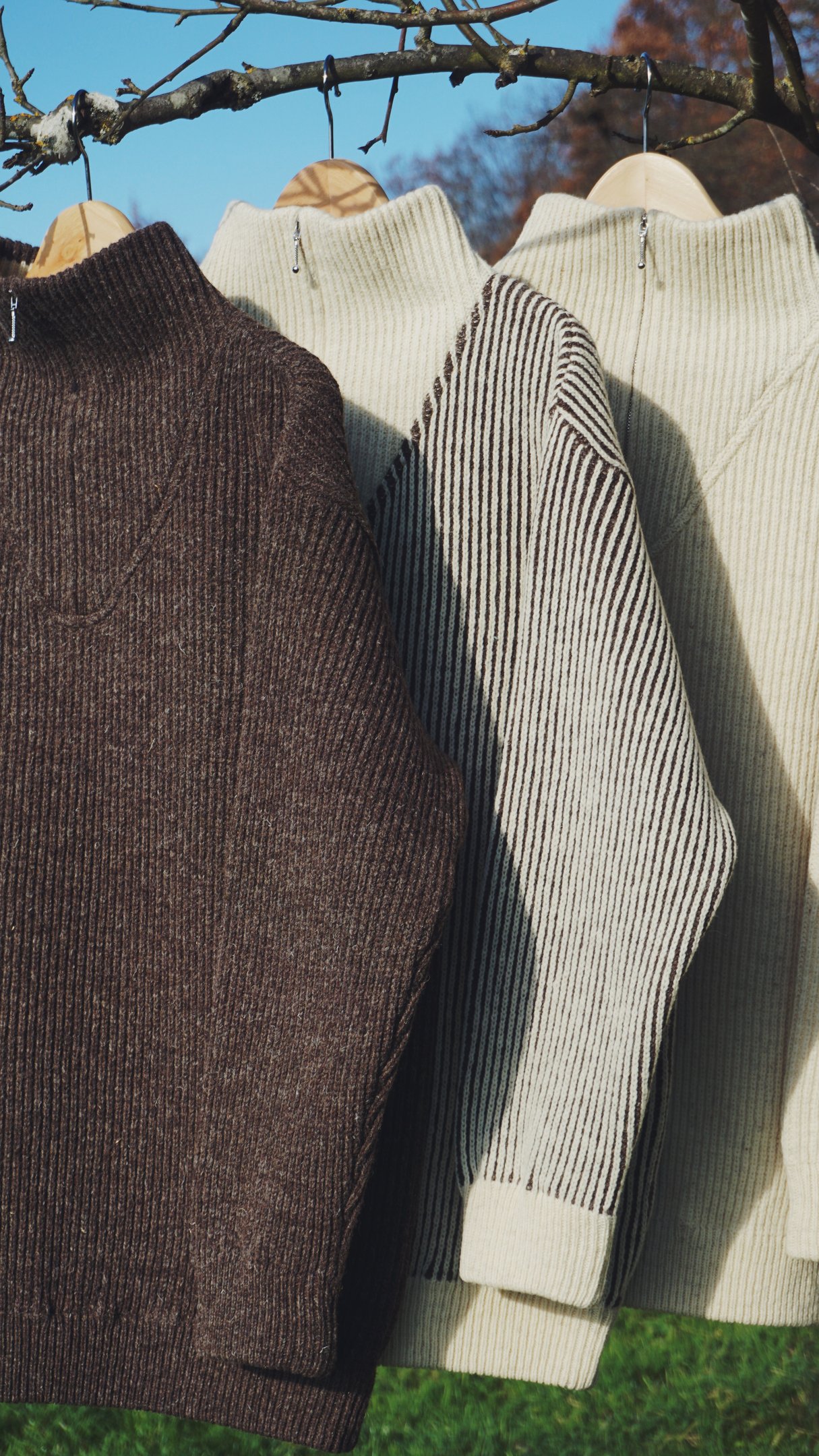 drei Troyer der Marke piies hängen auf einem Kleiderbügel in der Natur, ein dunkler, ein gestreifter